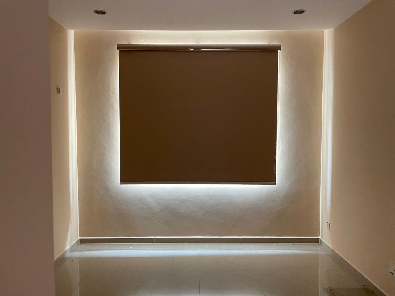Brown blackout roller blind set into a cove-lit feature wall over a glossy-floored room