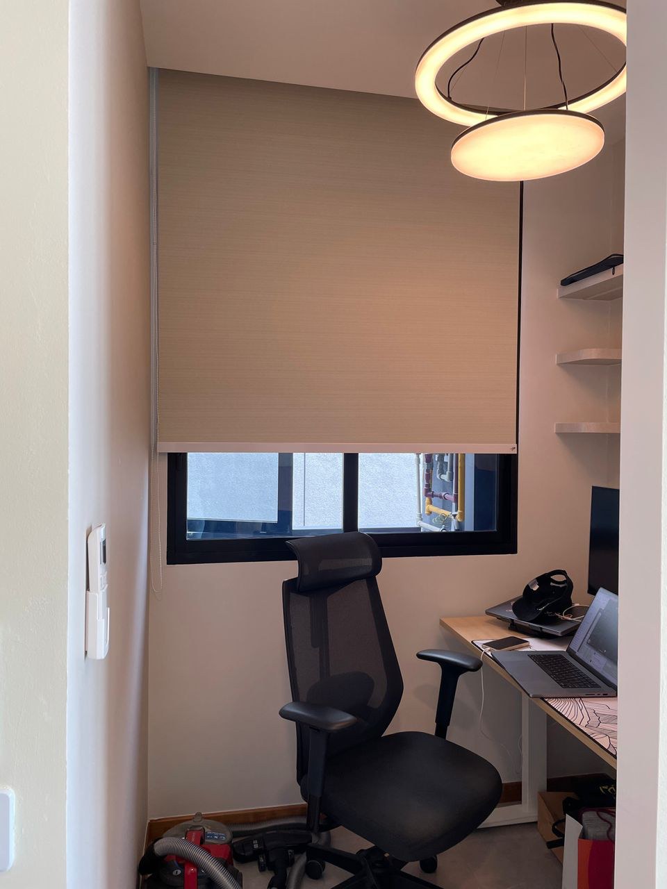 Beige sunscreen roller blind half-lowered over the window of a compact home office